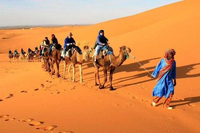 Eine Kamelkarawane, angeführt von einem Mann in blauem Gewand, über goldenem Sand