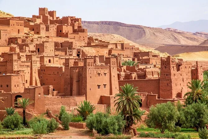 Torres de una kasbah de adobe entre palmeras con montañas detrás