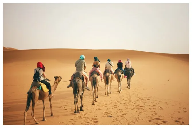 Reiter mit Kopftüchern auf einer Kamelreihe, die hellen Sand durchquert
