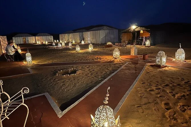 A desert camp at night lit by lanterns on the sand