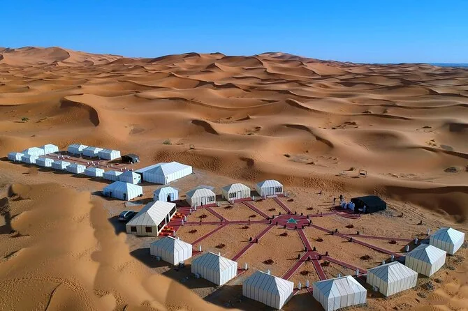 Aerial view of a camp of white tents around a courtyard in the dunes