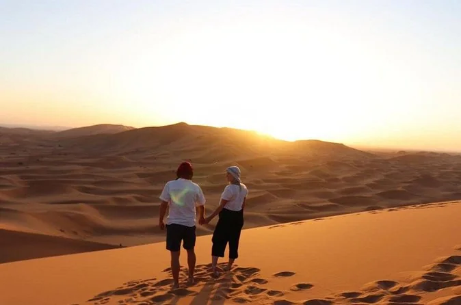 Dos viajeros vistos de espaldas contemplando la puesta de sol sobre las dunas